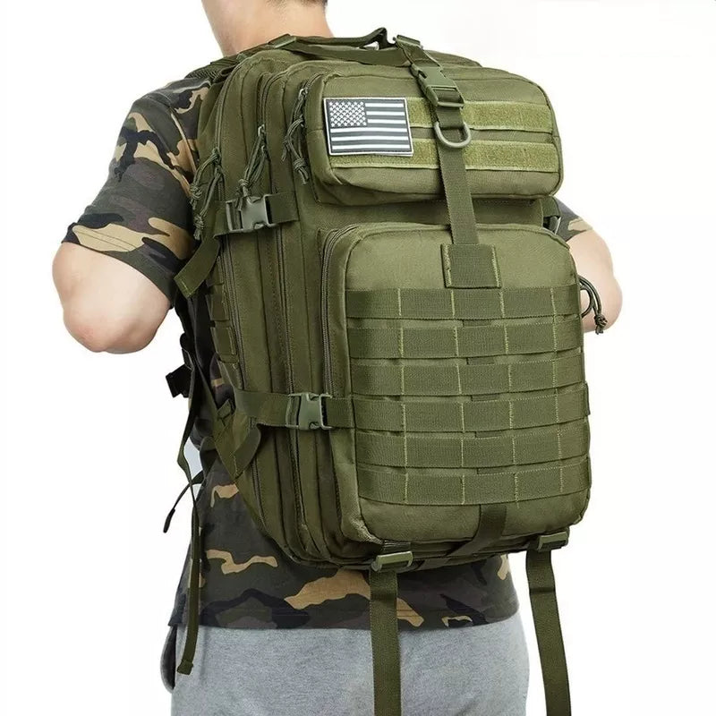 Mochila táctica de airsoft en verde militar, equipada con sistema MOLLE y parche de bandera estadounidense, perfecta para operaciones extensas y transporte de equipo.